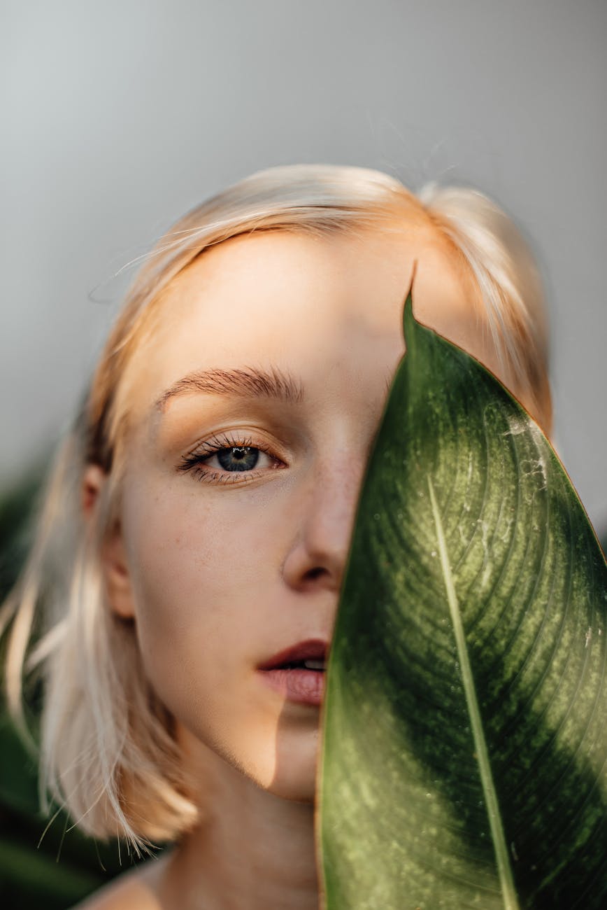 a woman covering half of her face with a leaf